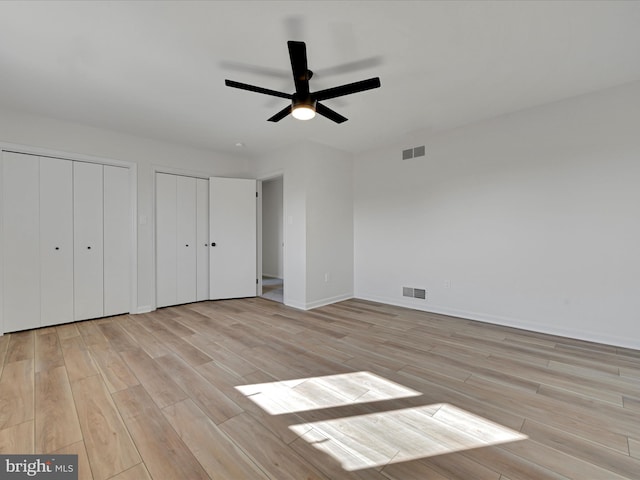 unfurnished bedroom featuring multiple closets, ceiling fan, and light wood-type flooring