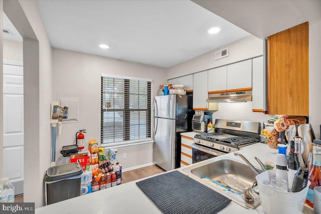 kitchen with stainless steel appliances, white cabinetry, sink, and light wood-type flooring