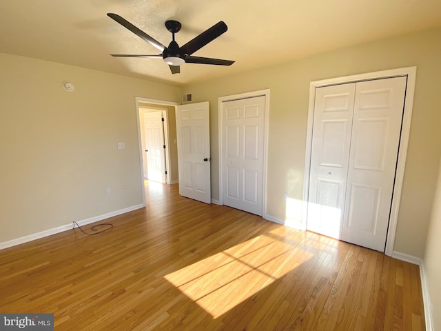 unfurnished bedroom with ceiling fan, wood-type flooring, and multiple closets