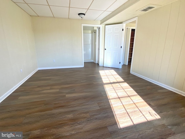 spare room with a paneled ceiling and dark hardwood / wood-style flooring