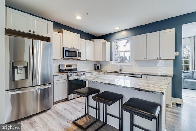 kitchen with appliances with stainless steel finishes, white cabinetry, sink, a center island, and light stone counters