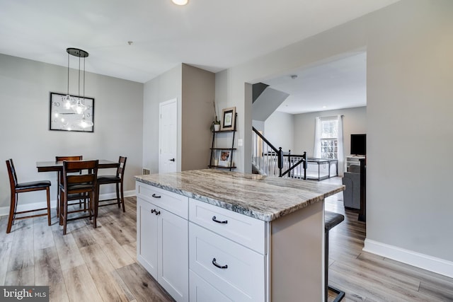 kitchen featuring a kitchen island, pendant lighting, white cabinetry, light stone counters, and light wood-type flooring