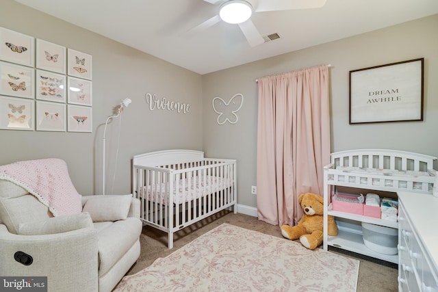 carpeted bedroom with a crib and ceiling fan