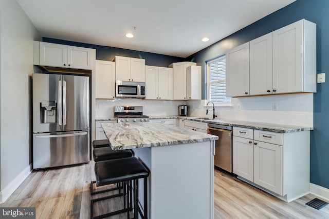 kitchen with a kitchen island, appliances with stainless steel finishes, white cabinetry, sink, and light stone counters