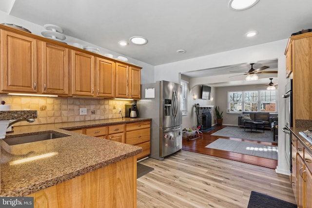 kitchen with sink, backsplash, stainless steel fridge with ice dispenser, dark stone counters, and light wood-type flooring