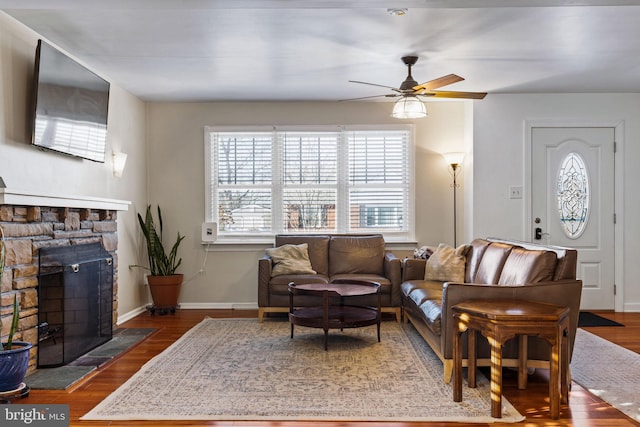 living room with ceiling fan, a stone fireplace, and dark hardwood / wood-style flooring