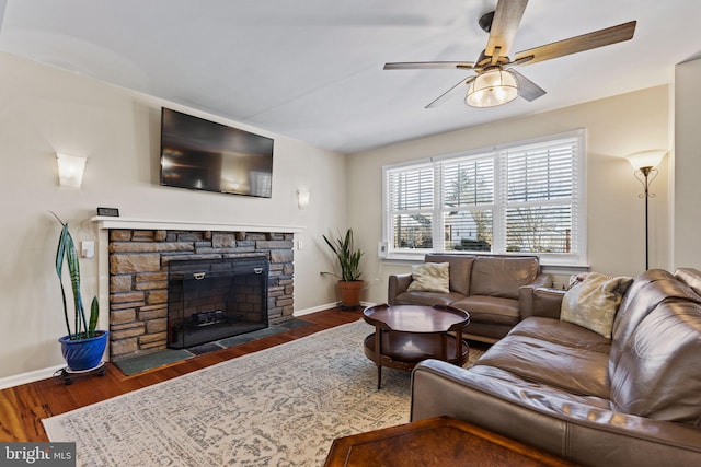 living room with dark hardwood / wood-style flooring, a stone fireplace, and ceiling fan