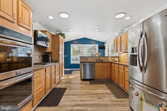 kitchen with vaulted ceiling, appliances with stainless steel finishes, kitchen peninsula, light hardwood / wood-style floors, and decorative backsplash