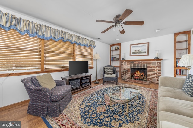 living area featuring a fireplace, wood finished floors, visible vents, baseboards, and a ceiling fan