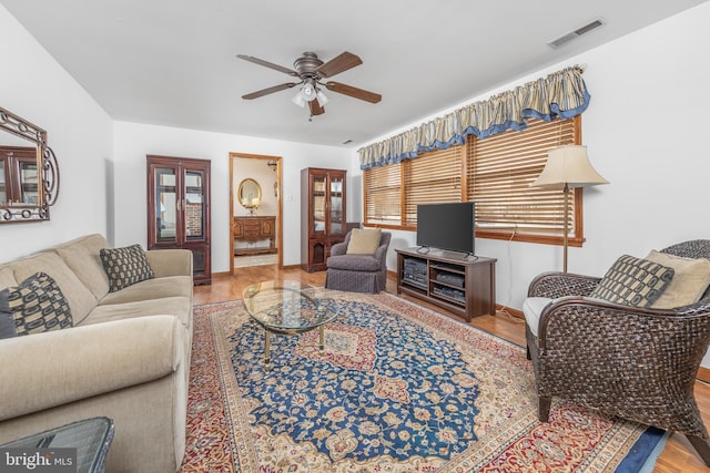 living room with a ceiling fan, visible vents, baseboards, and wood finished floors