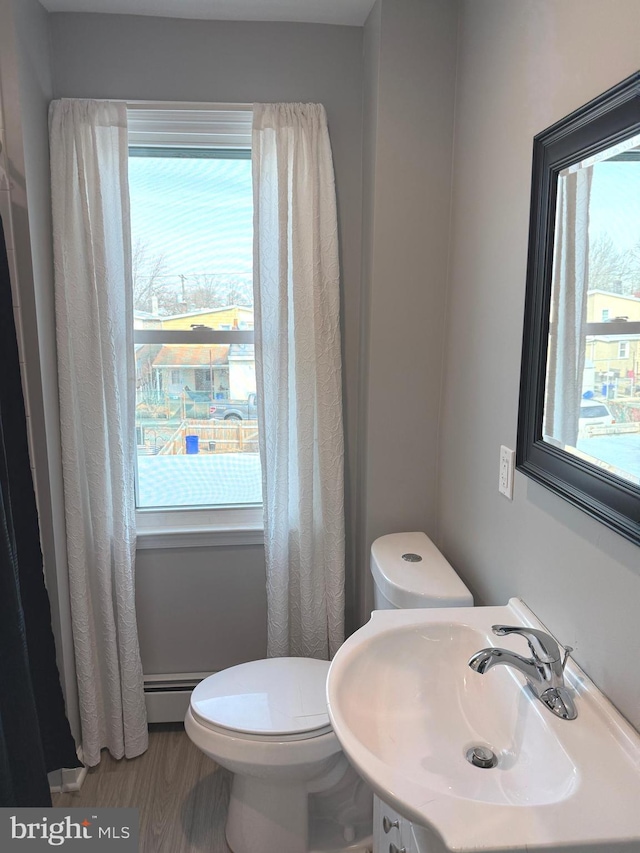 bathroom with hardwood / wood-style flooring, a baseboard radiator, sink, and toilet