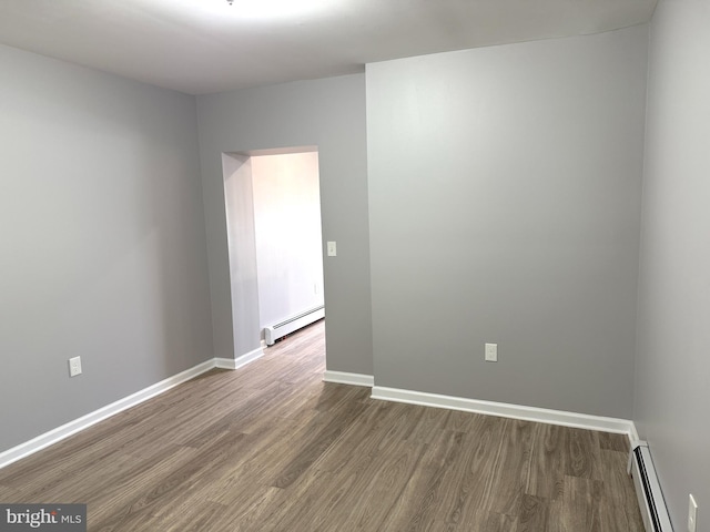 spare room with a baseboard heating unit and dark hardwood / wood-style flooring