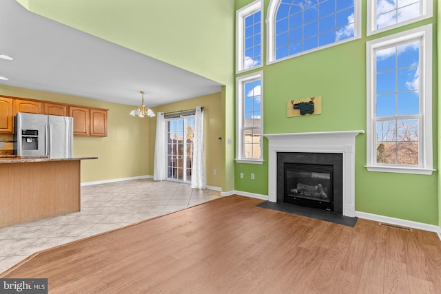 unfurnished living room with a towering ceiling, light hardwood / wood-style floors, and a chandelier