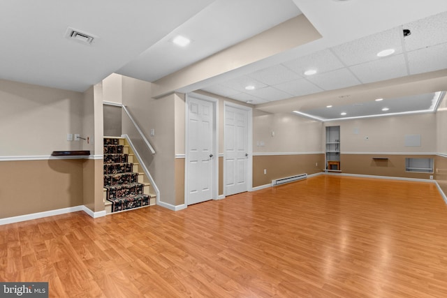 basement featuring a baseboard radiator, a drop ceiling, and light hardwood / wood-style floors