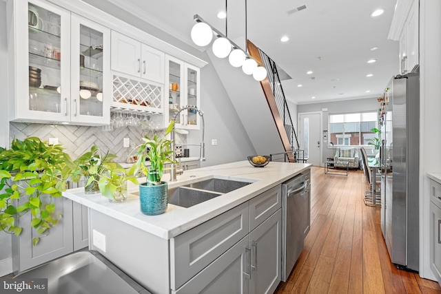 kitchen with appliances with stainless steel finishes, hardwood / wood-style floors, white cabinetry, hanging light fixtures, and ornamental molding