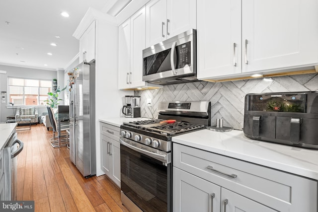 kitchen featuring crown molding, stainless steel appliances, tasteful backsplash, light stone countertops, and white cabinets