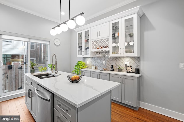 kitchen featuring sink, dishwasher, hanging light fixtures, light stone countertops, and an island with sink