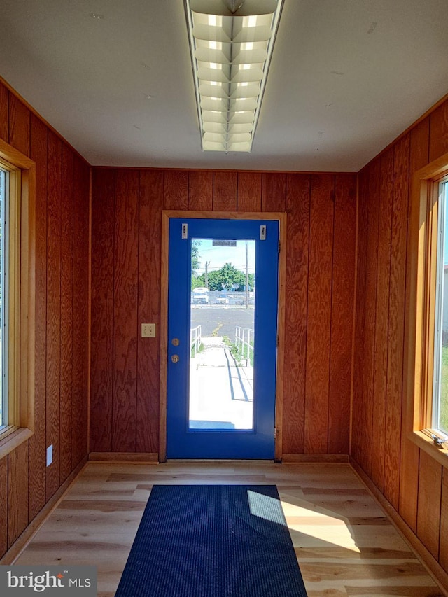 doorway to outside with light wood-style floors and wood walls