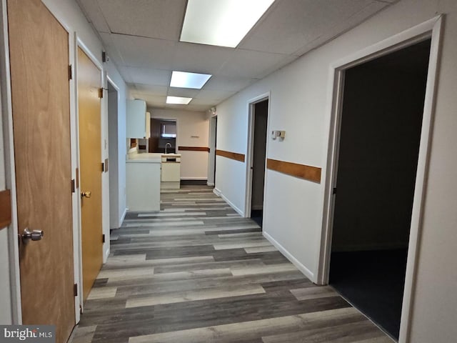 hall with a sink, baseboards, a drop ceiling, and wood finished floors