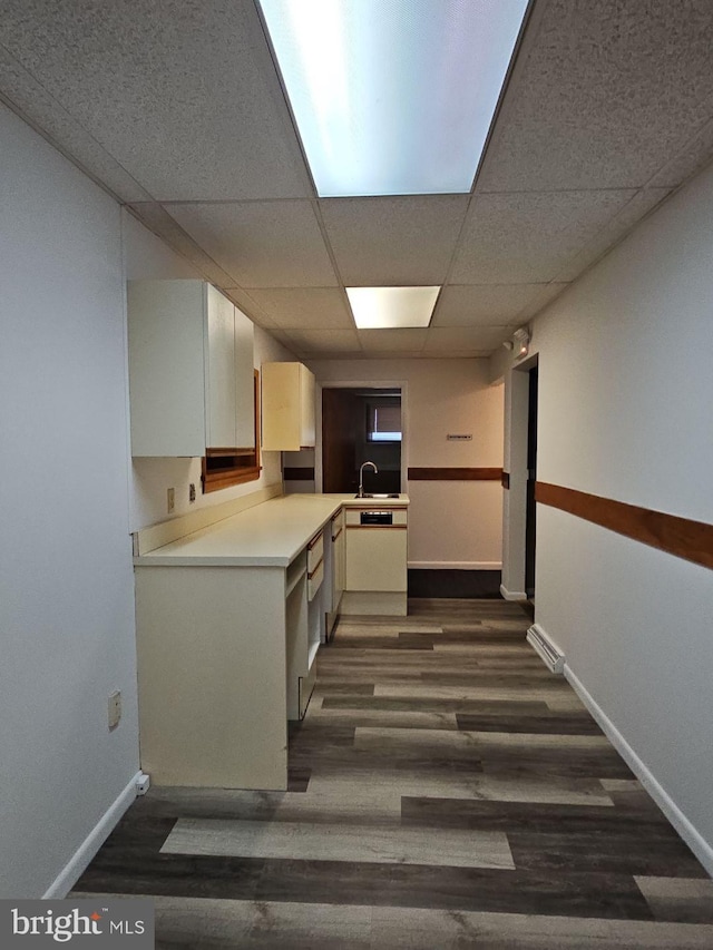 kitchen with baseboards, a drop ceiling, dark wood-style floors, light countertops, and a sink