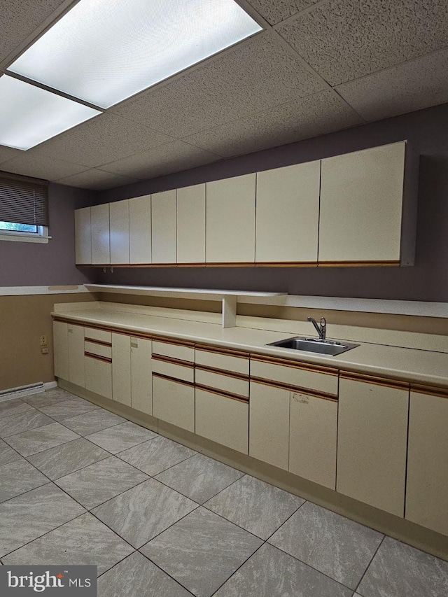 kitchen featuring cream cabinetry, light countertops, a sink, and a drop ceiling