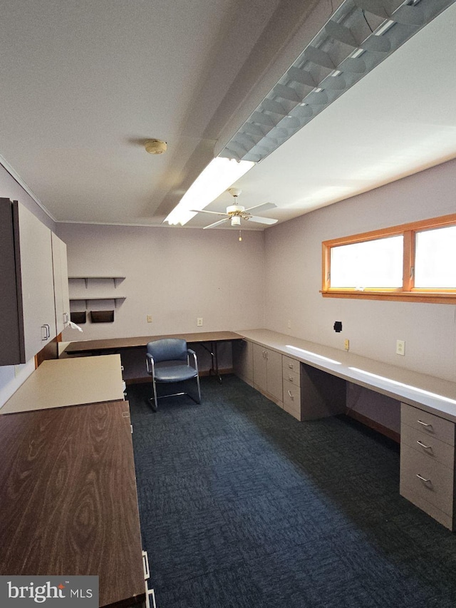 unfurnished office featuring ceiling fan, built in desk, and dark carpet