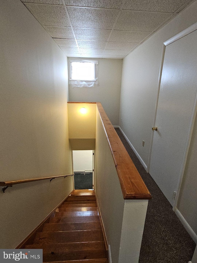 stairway with a drop ceiling, wood finished floors, and baseboards