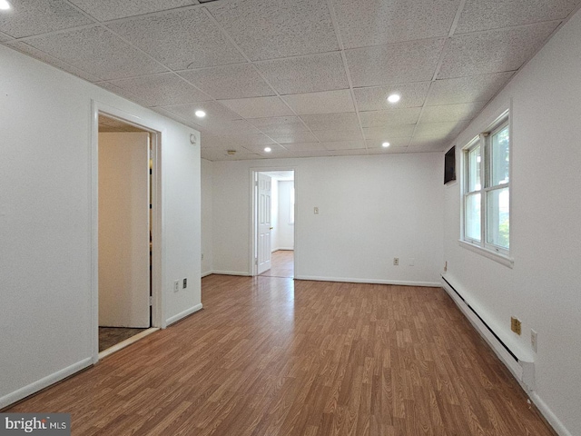 unfurnished room with baseboards, a drop ceiling, wood finished floors, baseboard heating, and recessed lighting