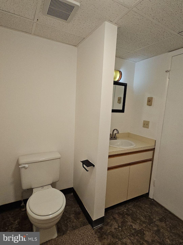 half bathroom with a paneled ceiling, visible vents, toilet, vanity, and baseboards