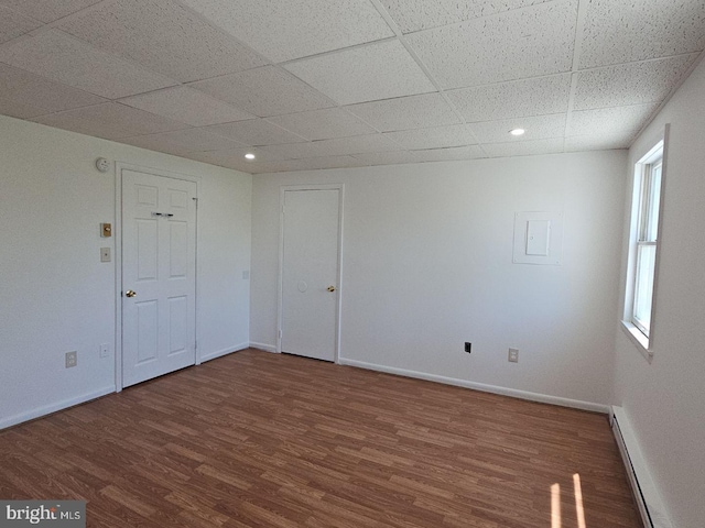 empty room with baseboards, dark wood finished floors, a drop ceiling, and baseboard heating