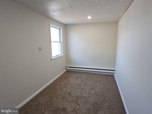 empty room with baseboard heating, a drop ceiling, carpet flooring, and baseboards