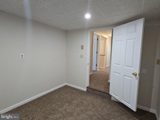 empty room with recessed lighting, a drop ceiling, dark carpet, and baseboards