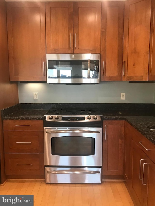 kitchen with appliances with stainless steel finishes, brown cabinetry, and dark stone countertops