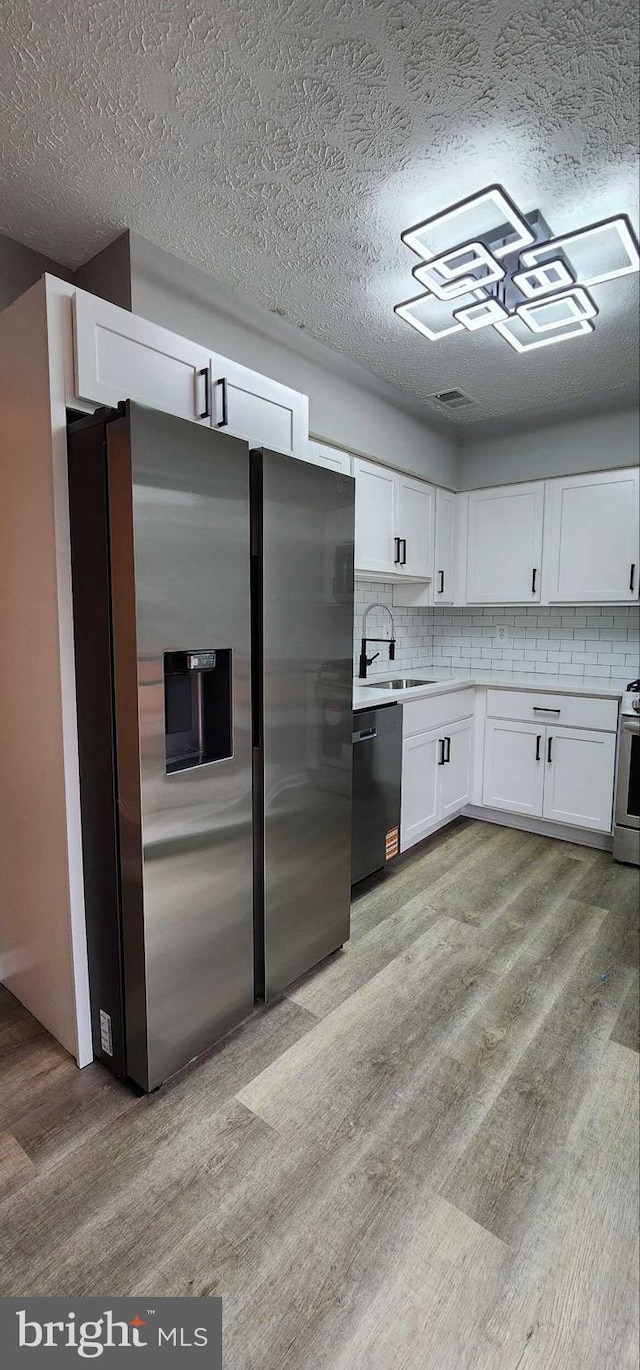 kitchen with light hardwood / wood-style flooring, stainless steel fridge, black dishwasher, tasteful backsplash, and white cabinets