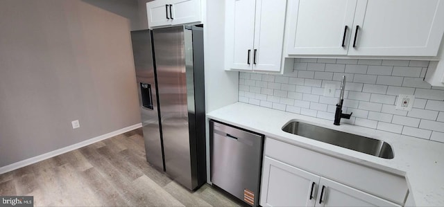 kitchen with sink, white cabinetry, light wood-type flooring, stainless steel appliances, and backsplash