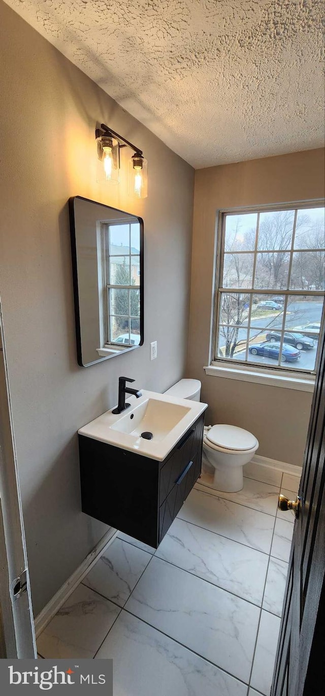 bathroom with vanity, plenty of natural light, toilet, and a textured ceiling