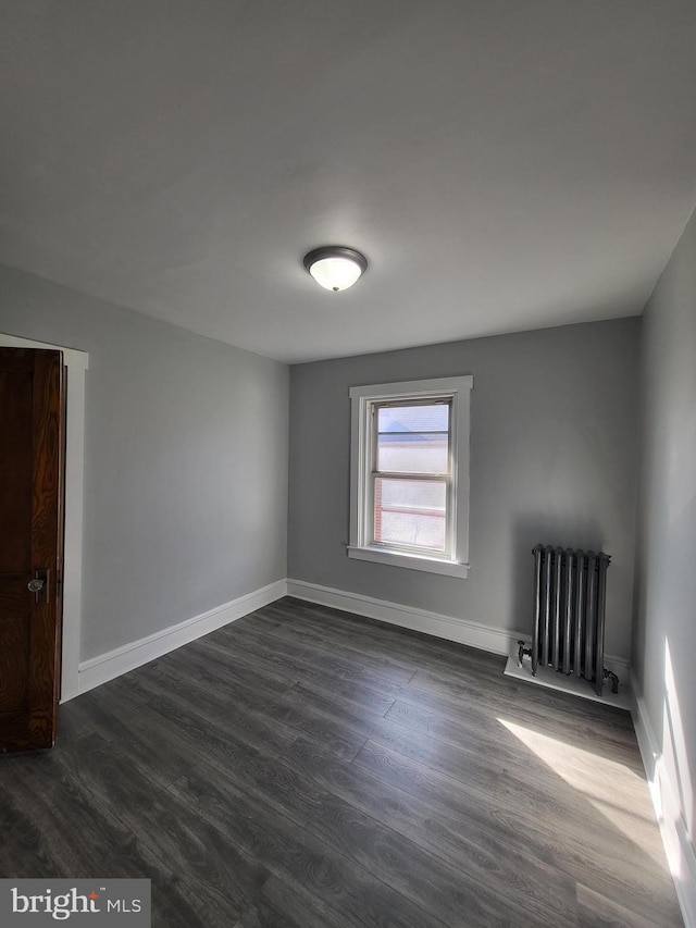 unfurnished room featuring radiator heating unit and dark hardwood / wood-style flooring