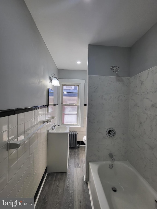 full bathroom featuring radiator, wood-type flooring, tile walls, vanity, and toilet