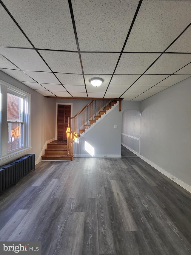 interior space with dark hardwood / wood-style flooring, radiator heating unit, and a drop ceiling