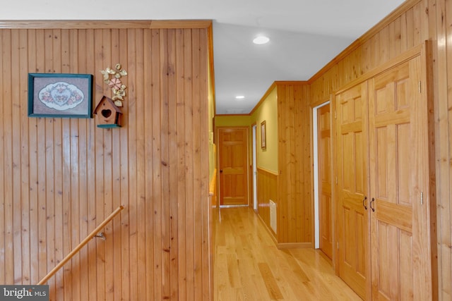 hallway with crown molding, light hardwood / wood-style flooring, and wooden walls