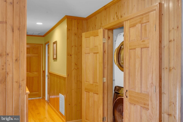 laundry room with stacked washer / drying machine, light hardwood / wood-style flooring, ornamental molding, and wood walls