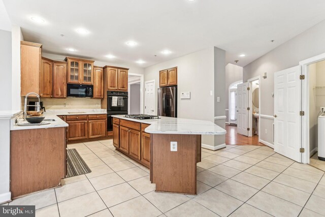 kitchen featuring brown cabinets, light tile patterned floors, glass insert cabinets, a kitchen island, and black appliances