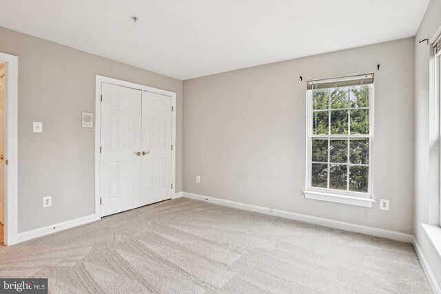 unfurnished bedroom with a closet, light colored carpet, and baseboards