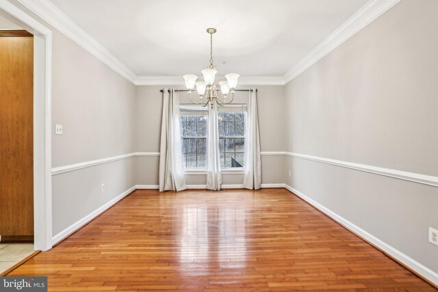 unfurnished dining area with a chandelier, ornamental molding, light wood-style flooring, and baseboards