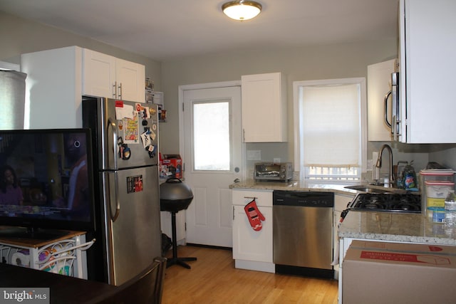 kitchen with light stone counters, light wood finished floors, stainless steel appliances, white cabinets, and a sink