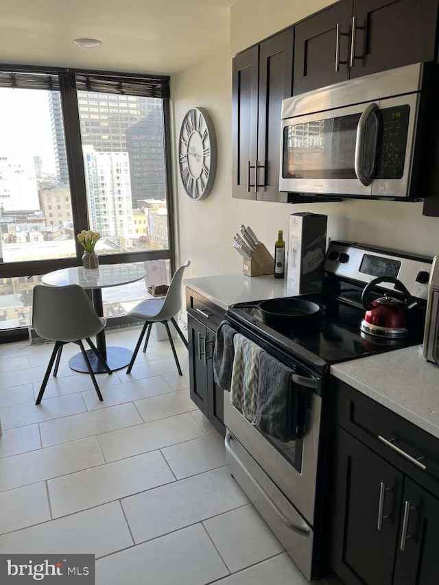 kitchen featuring dark brown cabinetry, appliances with stainless steel finishes, light tile patterned floors, and light stone counters