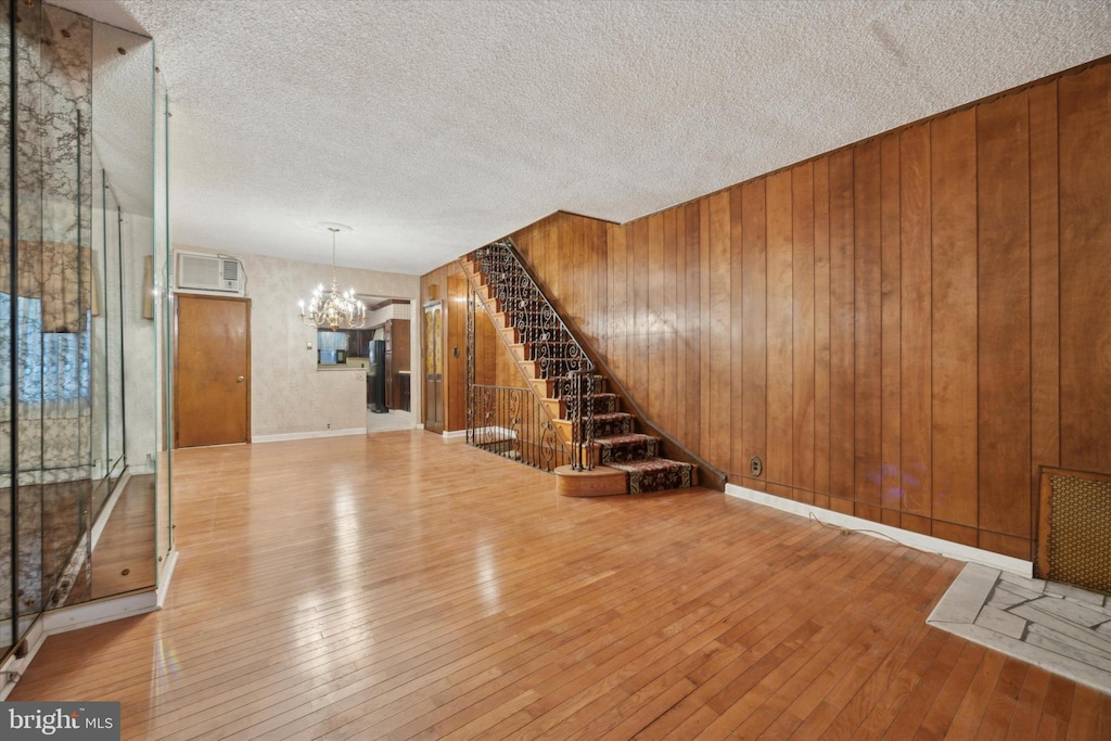 unfurnished living room with wooden walls, a chandelier, light hardwood / wood-style flooring, and a textured ceiling