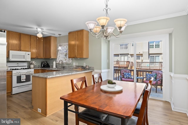 kitchen featuring brown cabinets, light wood-style flooring, a sink, white appliances, and a peninsula