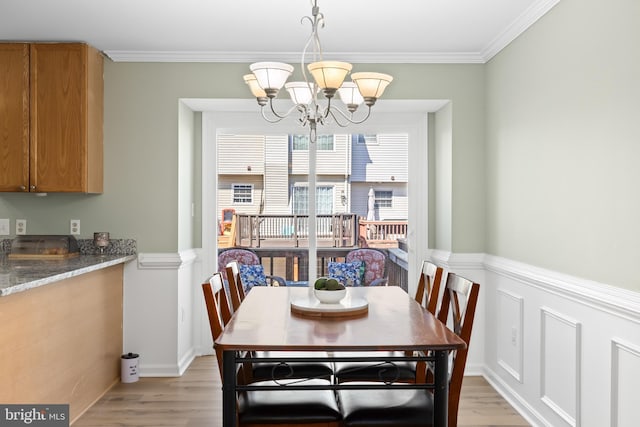 dining room featuring ornamental molding, wainscoting, light wood-style flooring, and an inviting chandelier