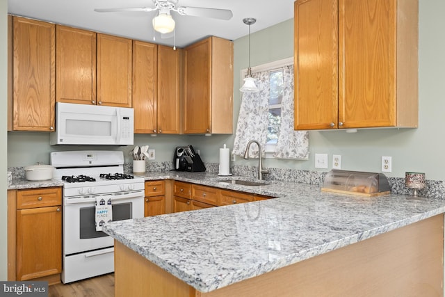 kitchen with a peninsula, white appliances, a sink, light stone countertops, and decorative light fixtures